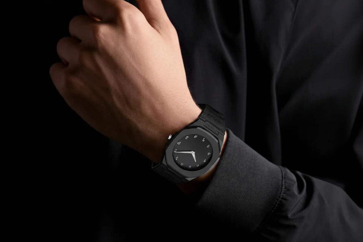 Minimalist black wristwatch with mesh strap on person's wrist, modern fashion accessory